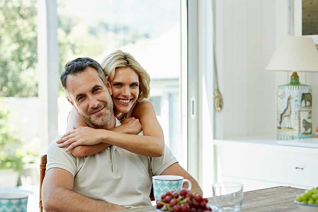 Portrait of smiling woman embracing man from behind at home